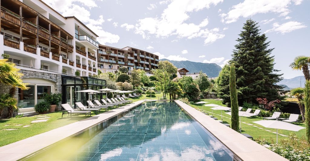 Infinity-Pool im Hohenwart Hotel in Südtirol mit Panoramablick auf die Berge, umgeben von Liegestühlen und Gartenanlage